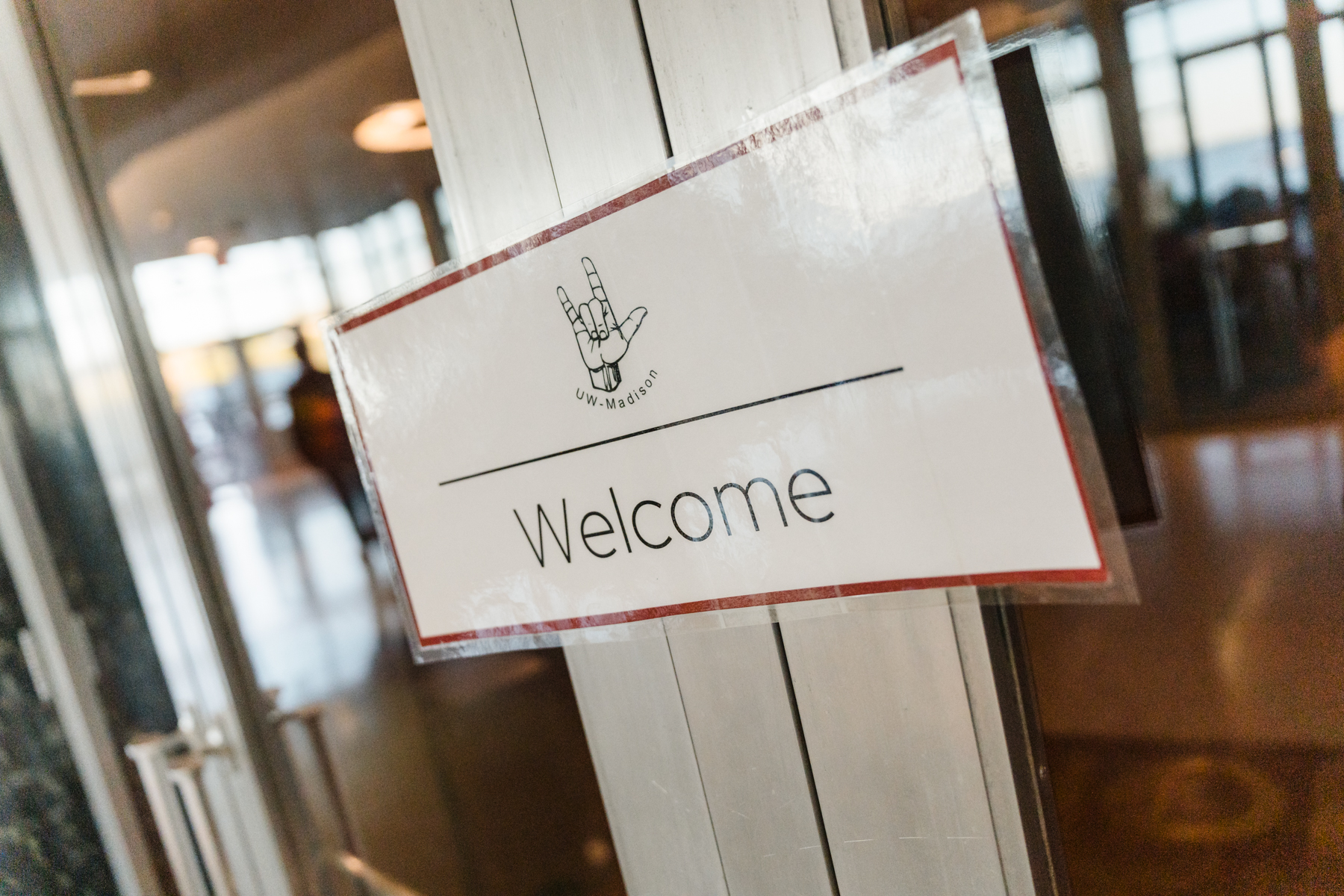 A sign on a door with the word "welcome" and an ASL icon.